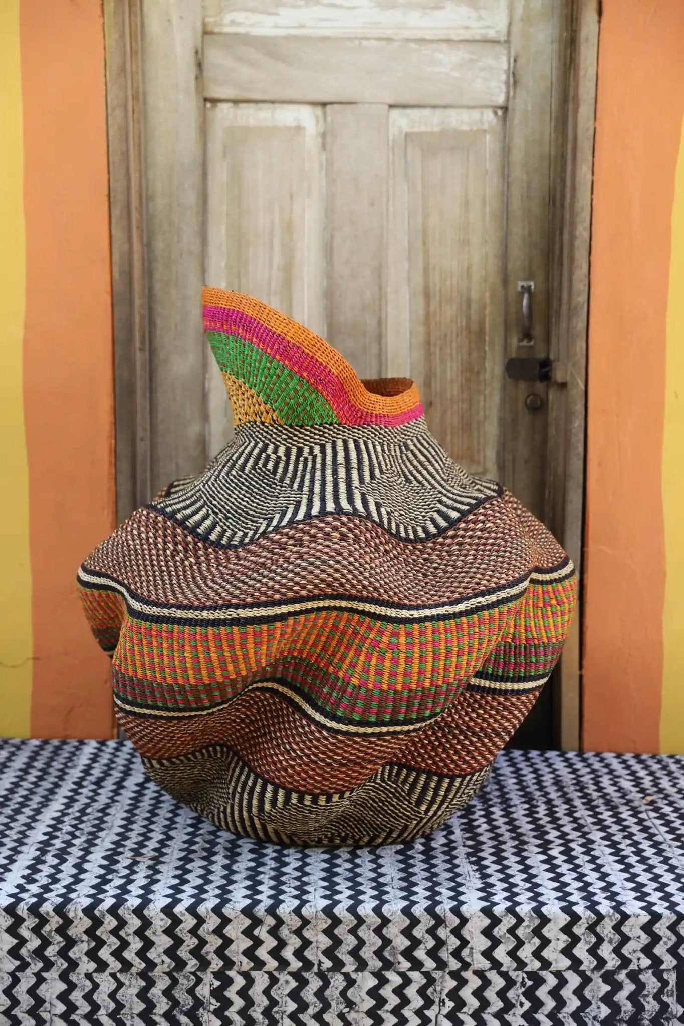 A colorful, handwoven piece with decorative curves sitting on a black and white cloth against a wooden door
