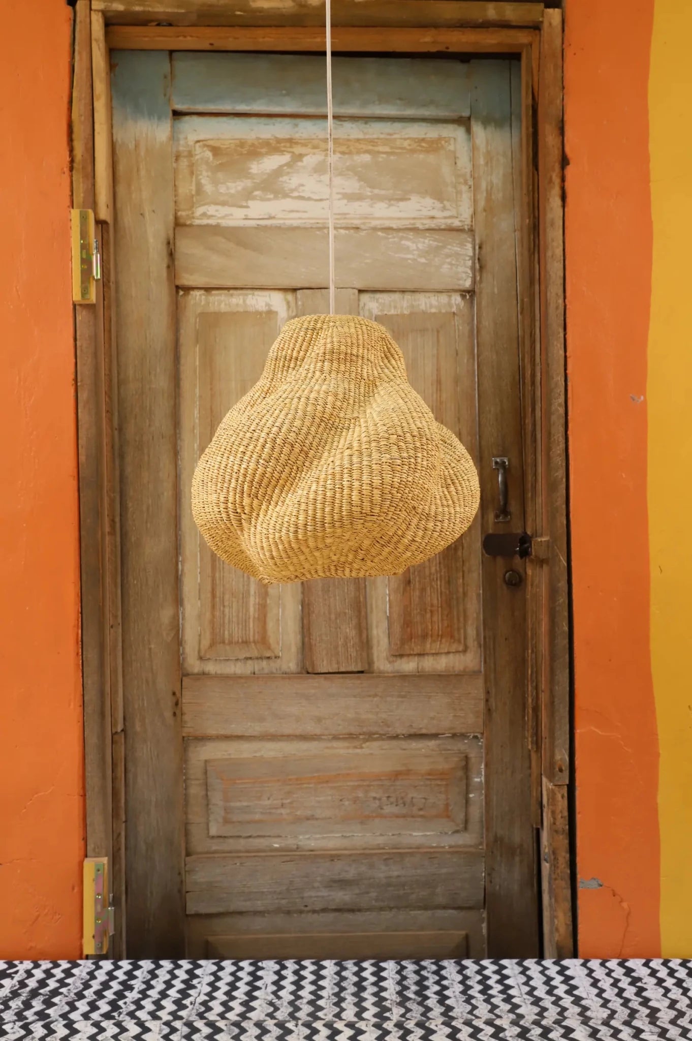 Woven pendant light hanging from a wooden door with an orange wall background