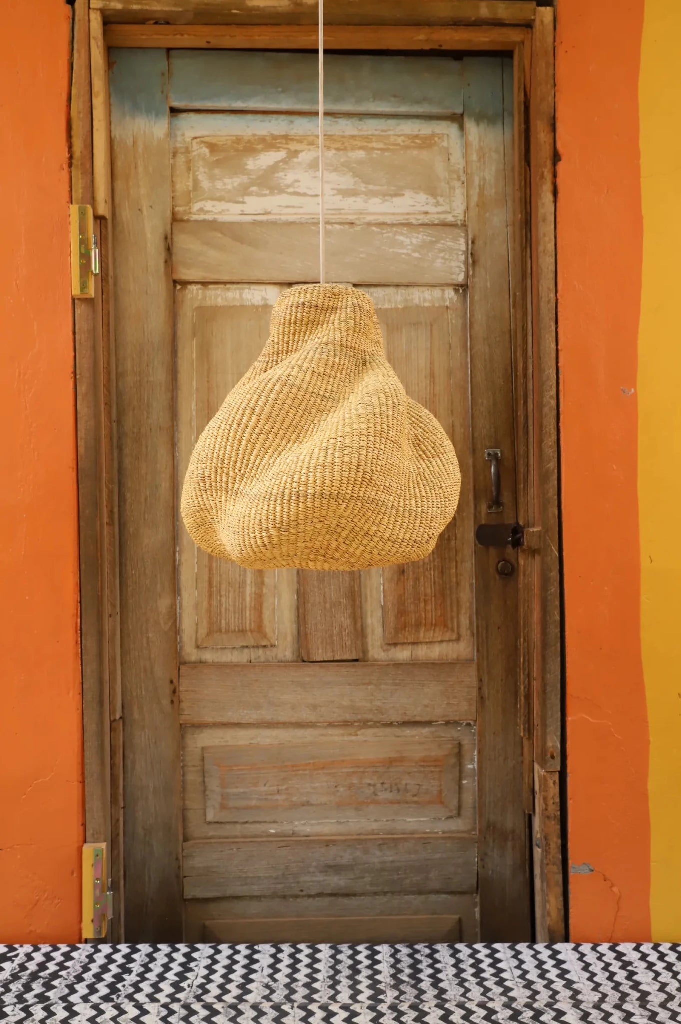 Woven basket light fixture hanging from a wooden door with an orange wall background