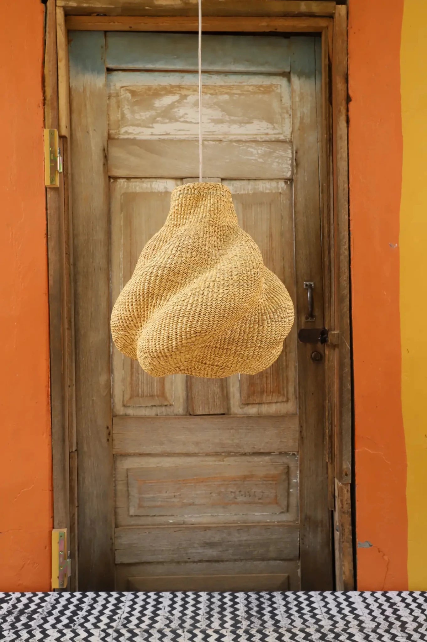Woven basket hanging from a string in front of a wooden door with an orange wall background.