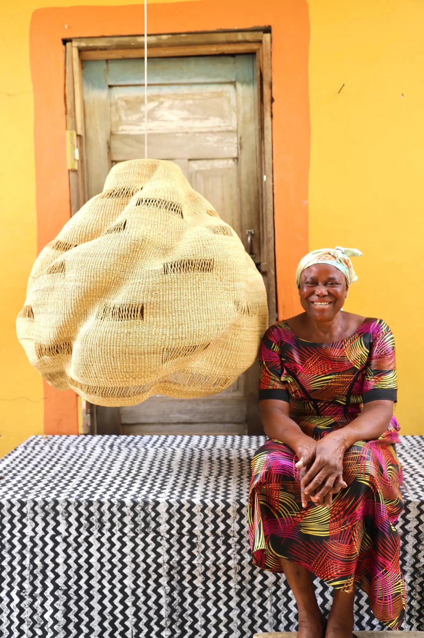 Woman sitting on a bench with a colorful dress against a yellow wall.