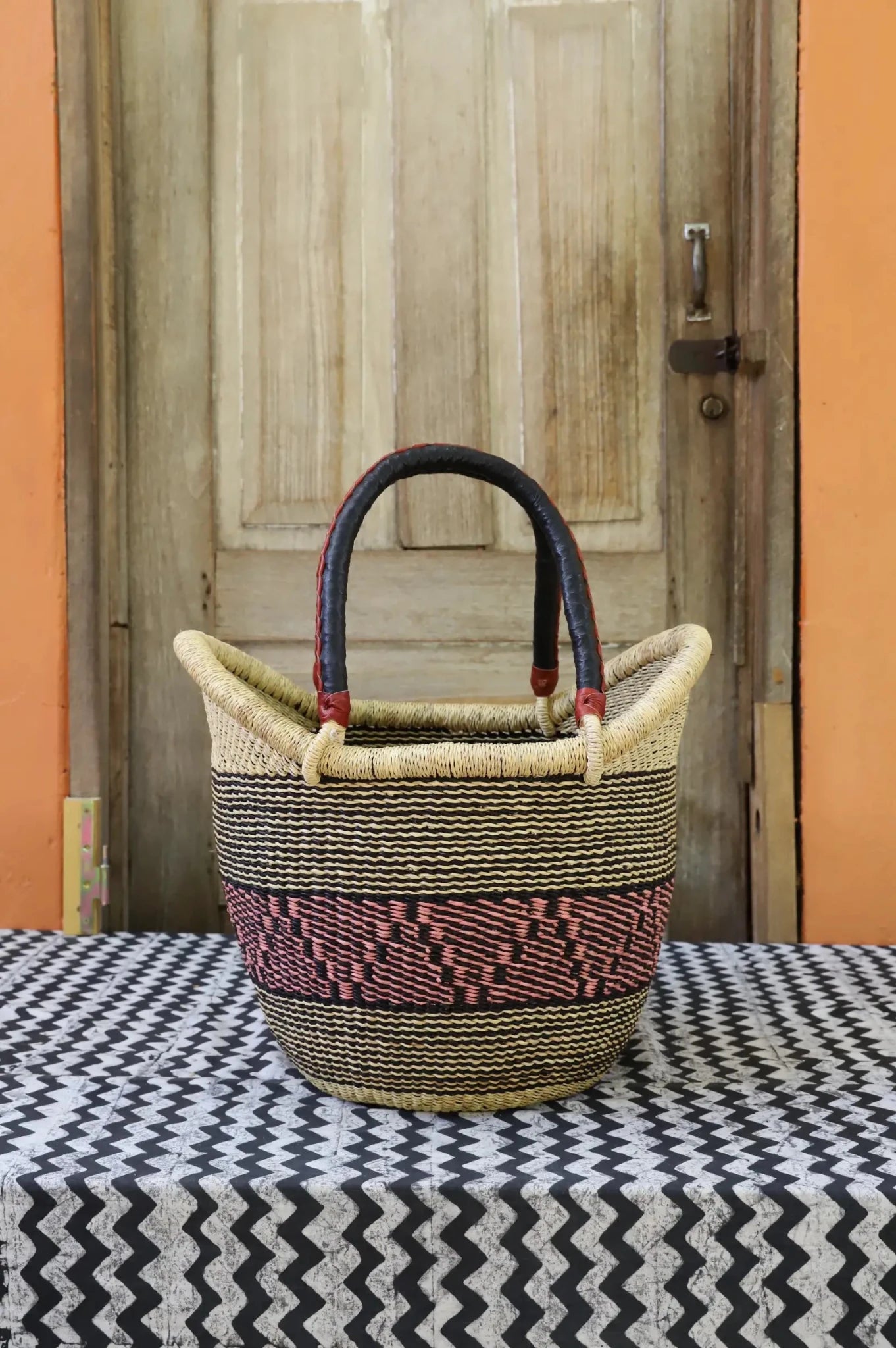 Woven carry on bag with premium leather handles on a black and white cloth against a wooden door.