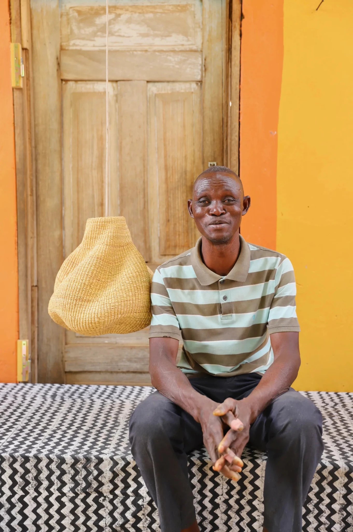 Man sitting on a black and white cloth  with a wooden door and yellow wall in the background