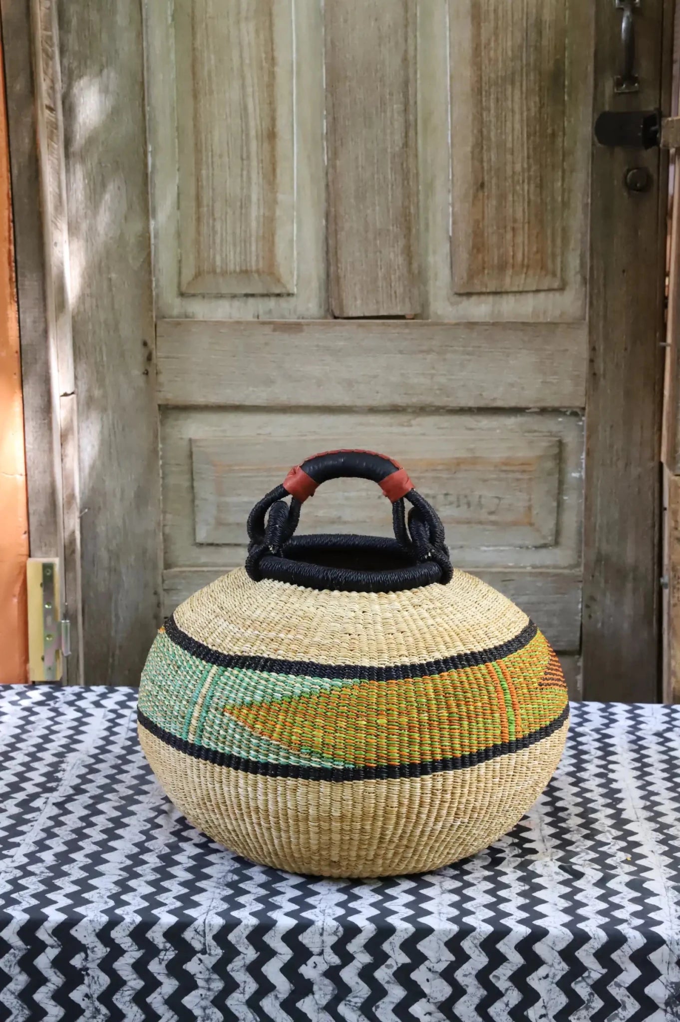 Colourful storage basket sitting on a black and white cloth against a wooden door.