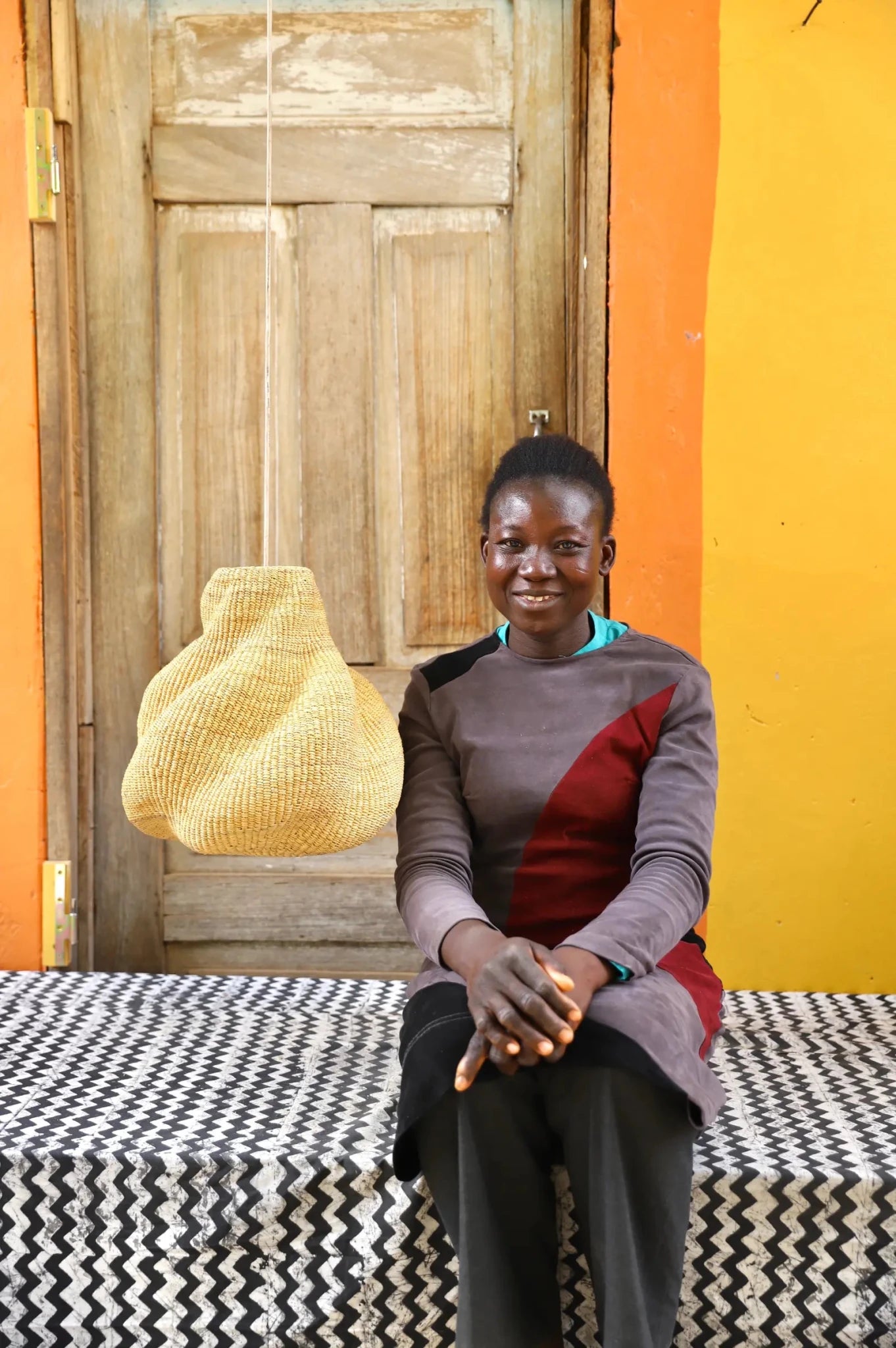 Woman sitting on a patterned black and white cloth against an orange wall with a woven basket.