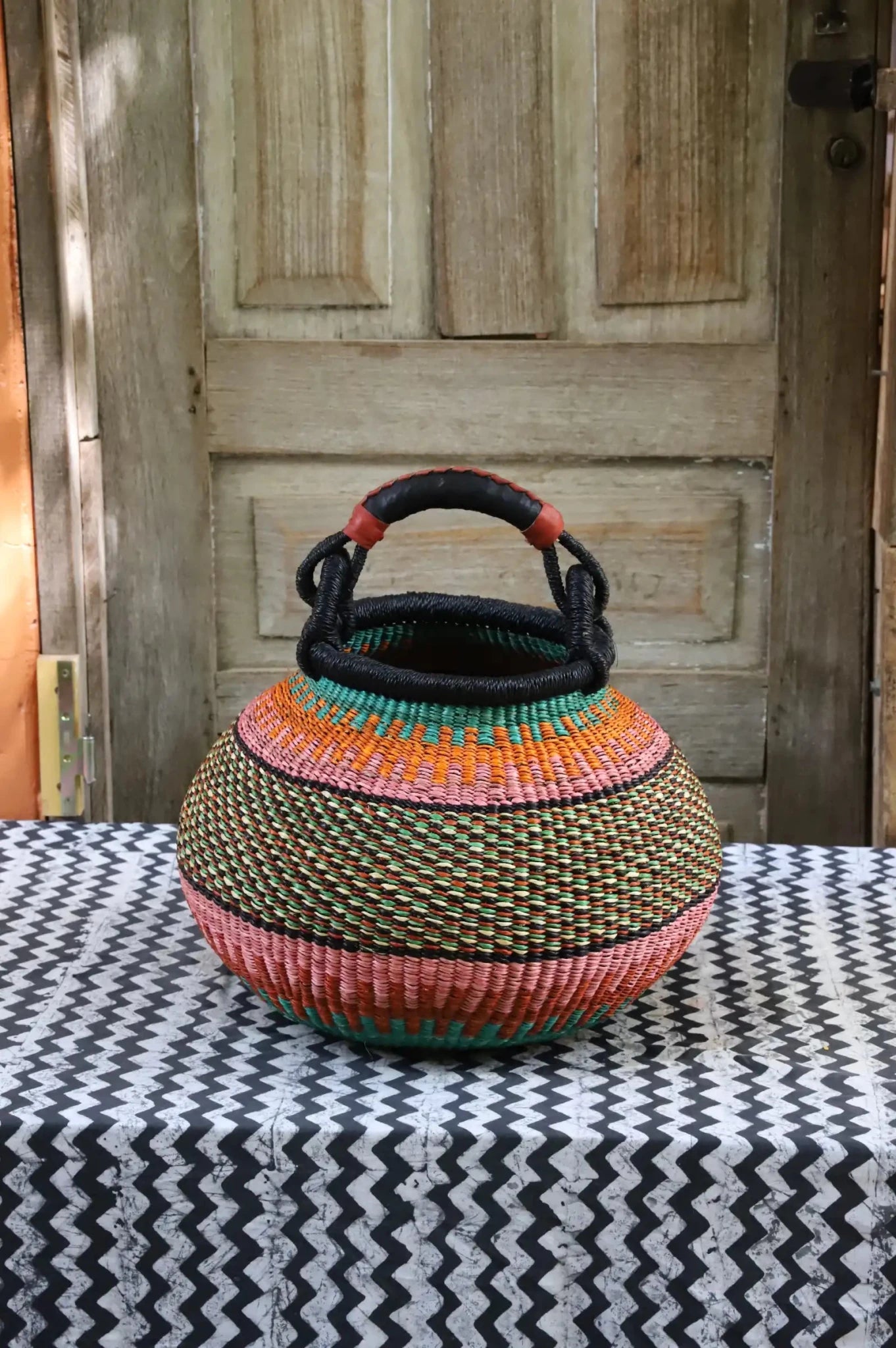 Colourful storage basket sitting on a black and white cloth against a wooden door.