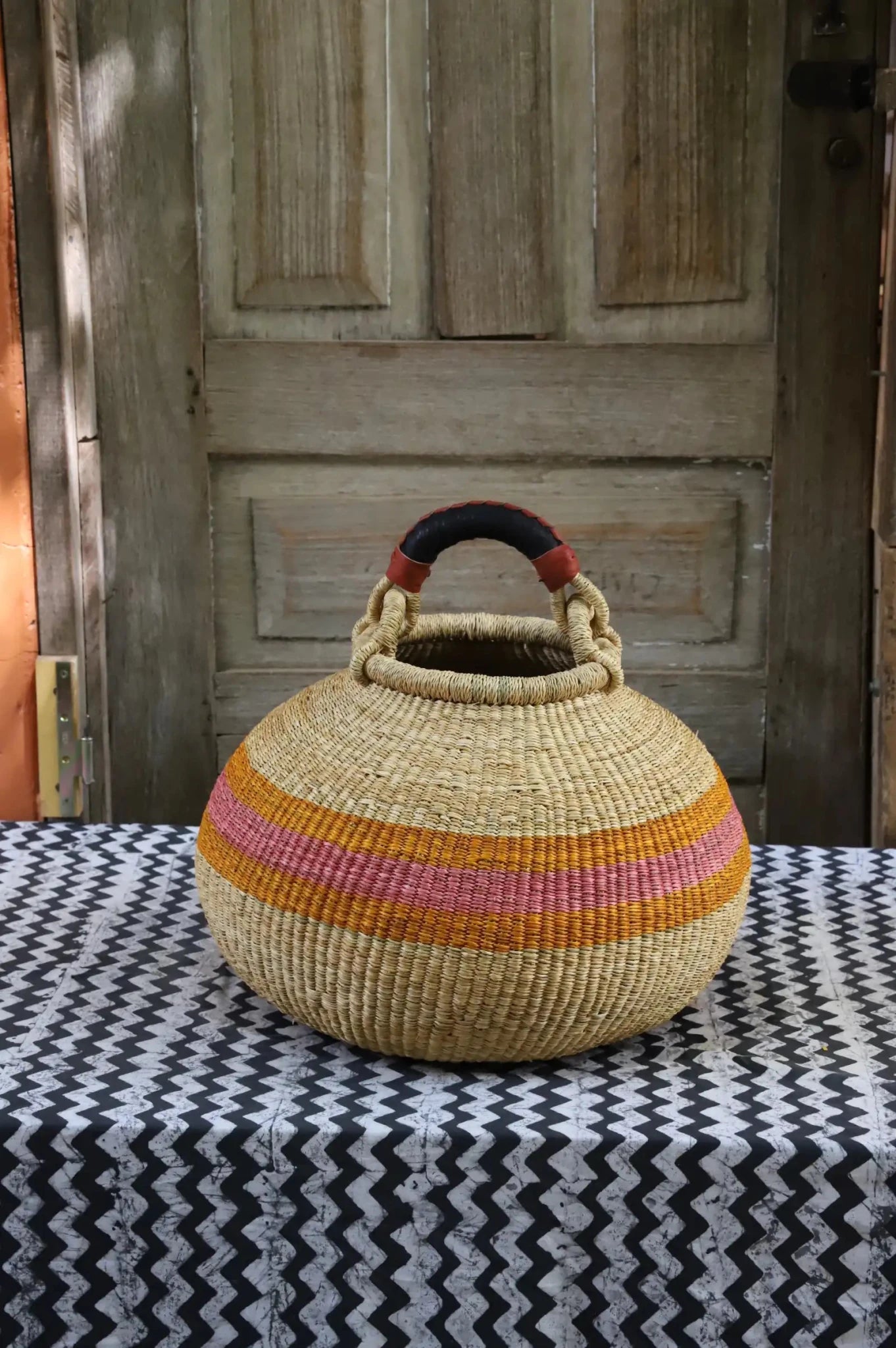 Colourful storage basket sitting on a black and white cloth against a wooden door.