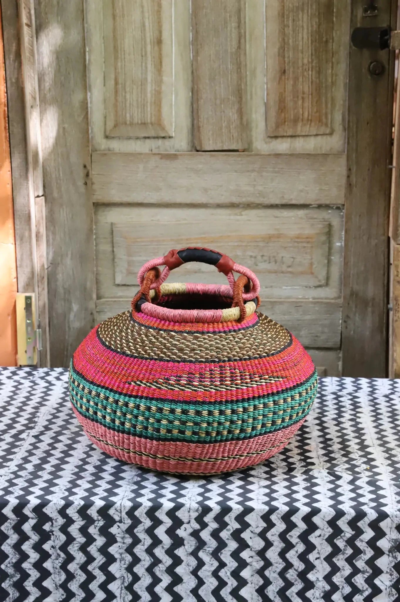 Colourful storage basket sitting on a black and white cloth against a wooden door.
