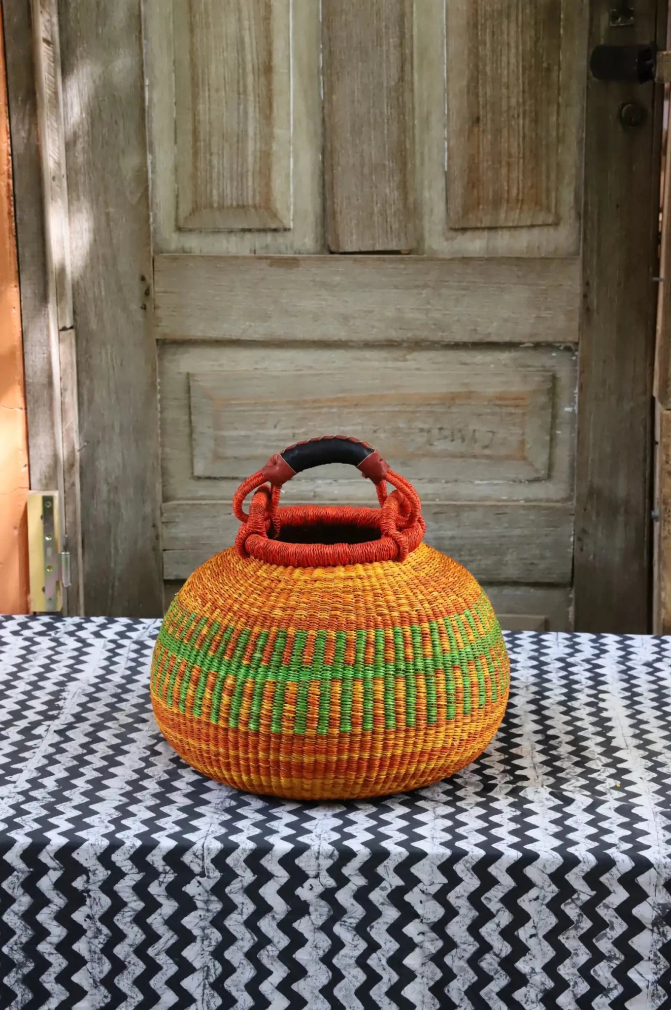 Colourful storage basket sitting on a black and white cloth against a wooden door.