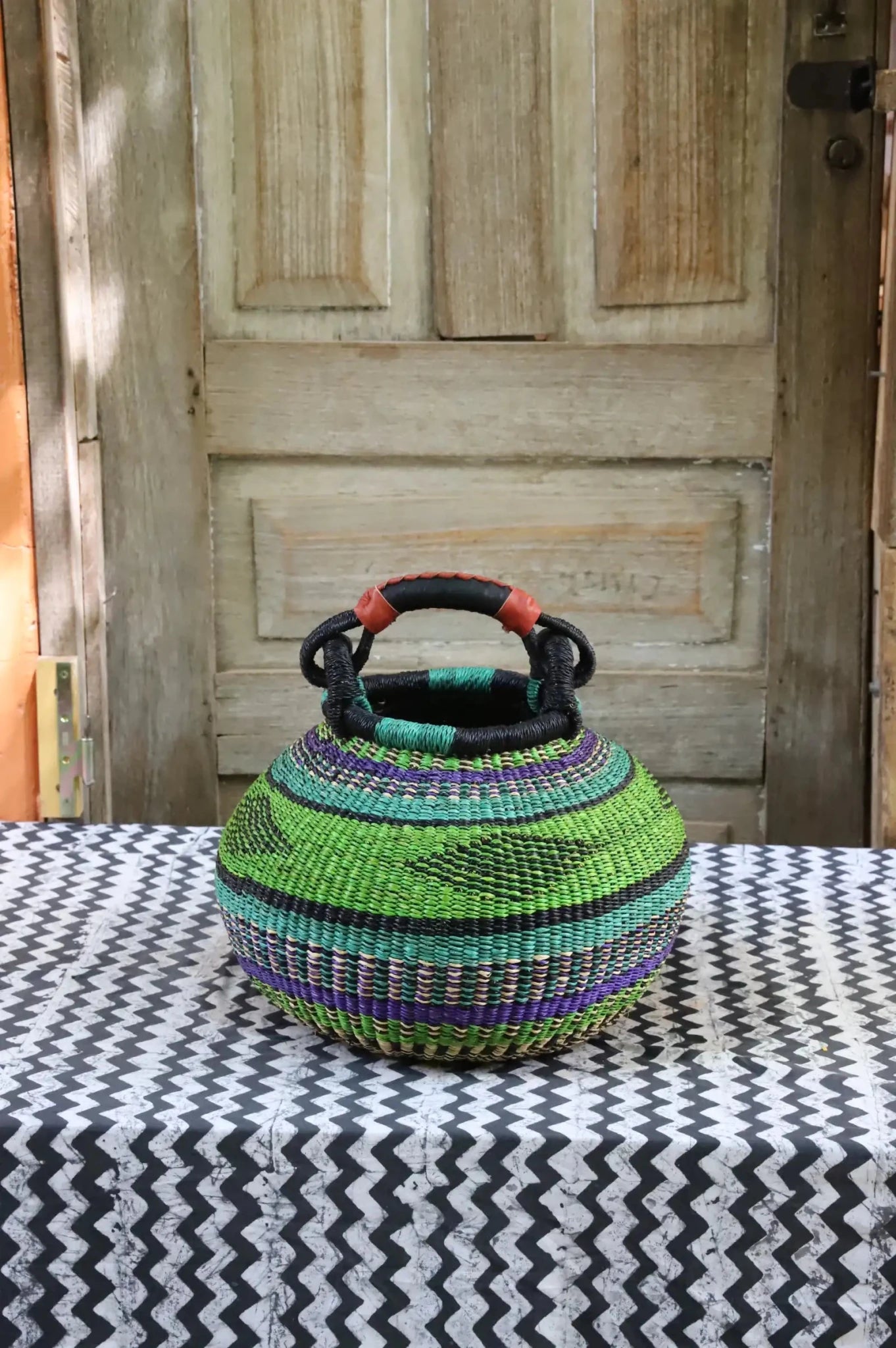 Colourful storage basket sitting on a black and white cloth against a wooden door.