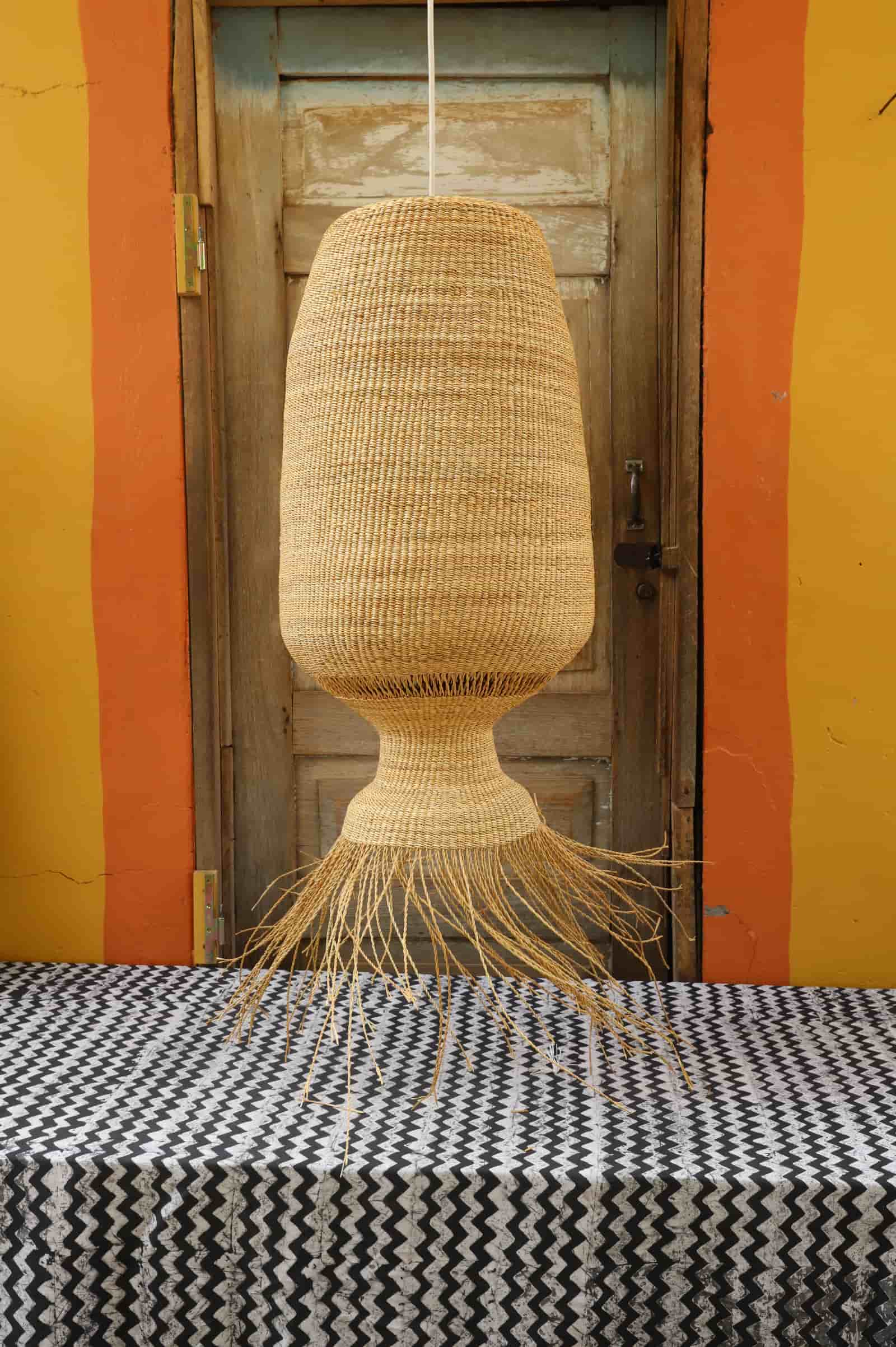 Woven lampshade with fringes on a table against a striped wall.