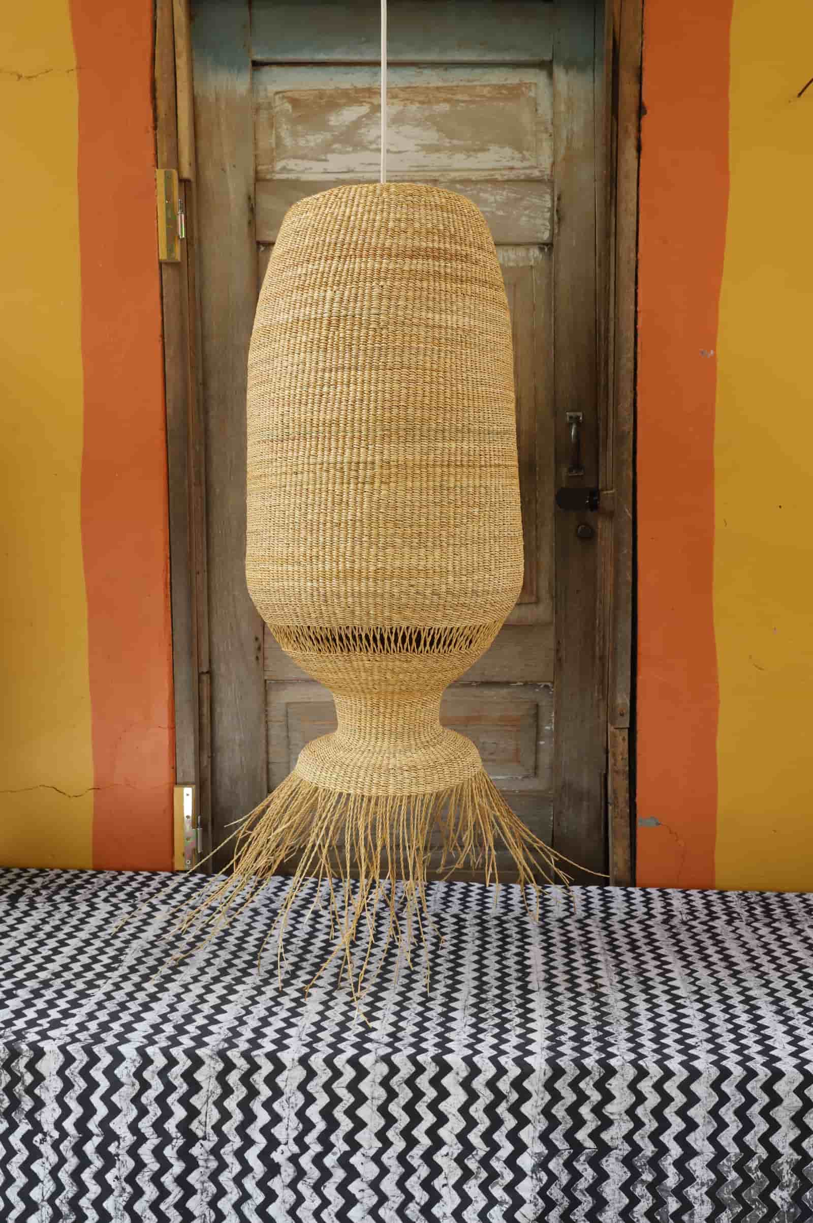 Woven lampshade hanging against a colourful striped wall and wooden door with black and white cloth