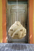 Textured bag hanging from a string in front of a wooden door with a colorful wall background.