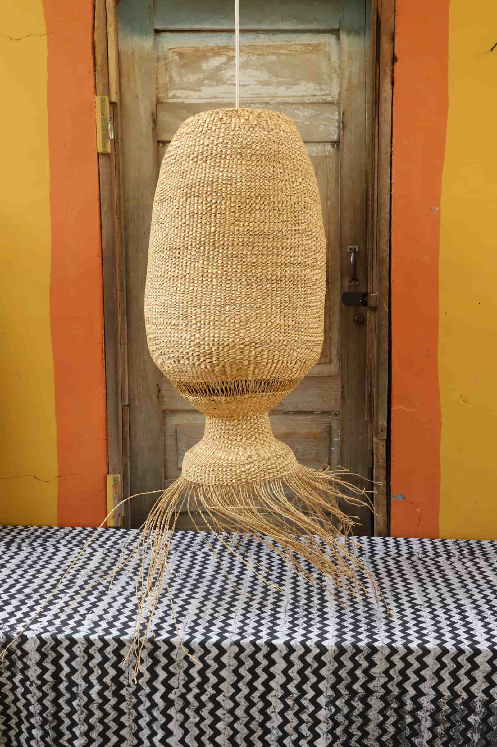 Woven lampshade hanging on a table with a striped wall background