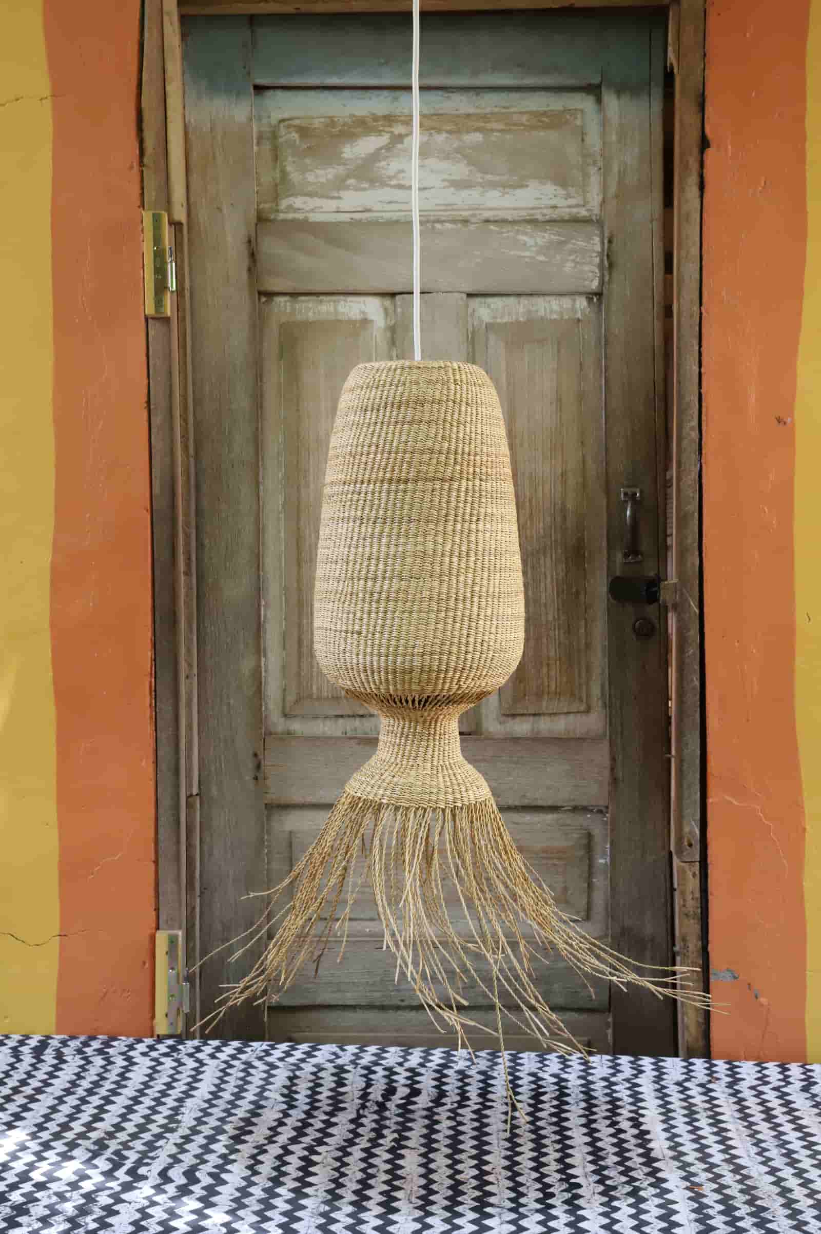 Woven pendant light hanging in front of a rustic wooden door with colorful walls.