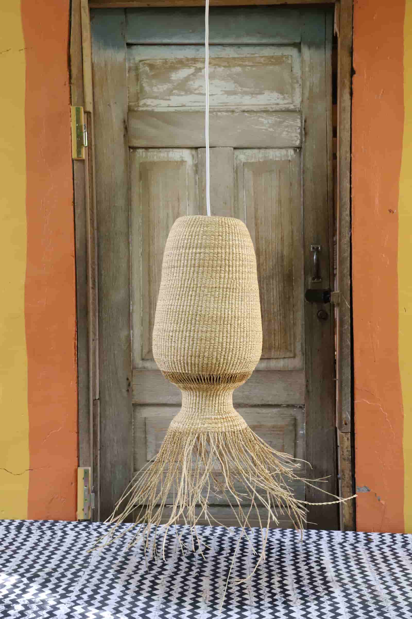 Woven lamp hanging in front of a wooden door with colorful walls.
