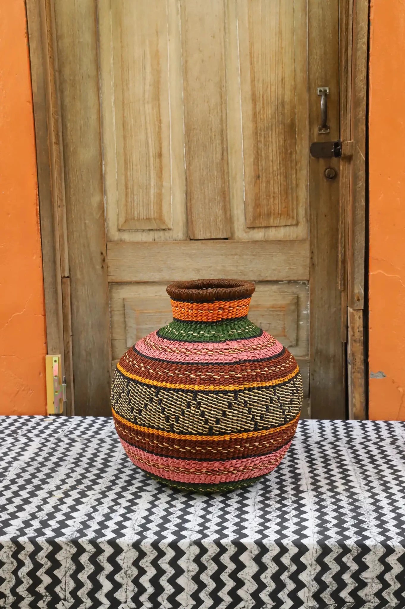 Decorative handwoven basket with colorful patterns on a black and white cloth against a wooden door.
