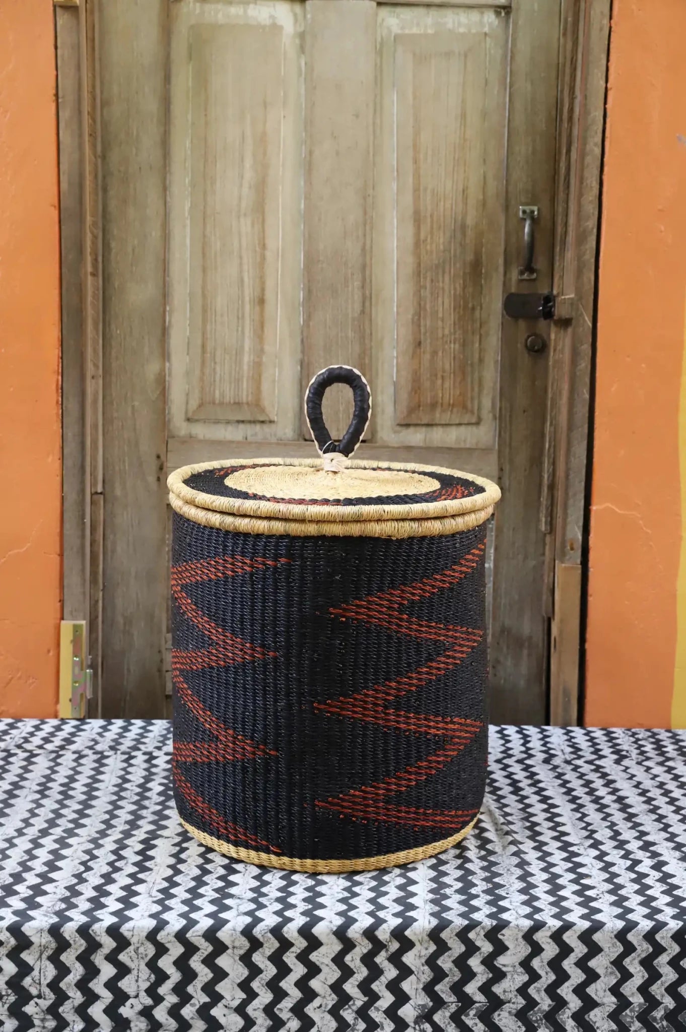 Woven basket with a lid on a table in front of a wooden door.