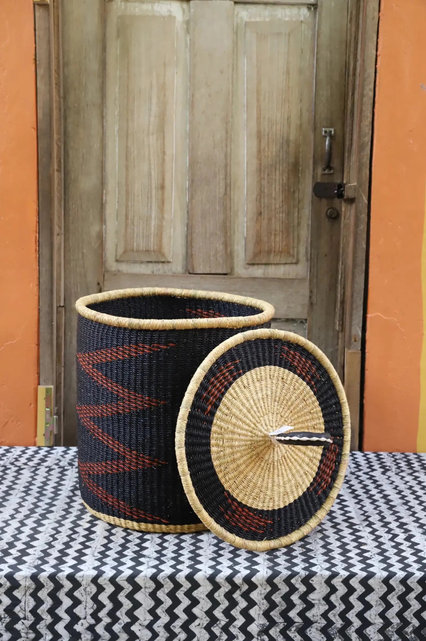 Woven baskets with black, red, and beige patterns on a table with a wooden door in the background.