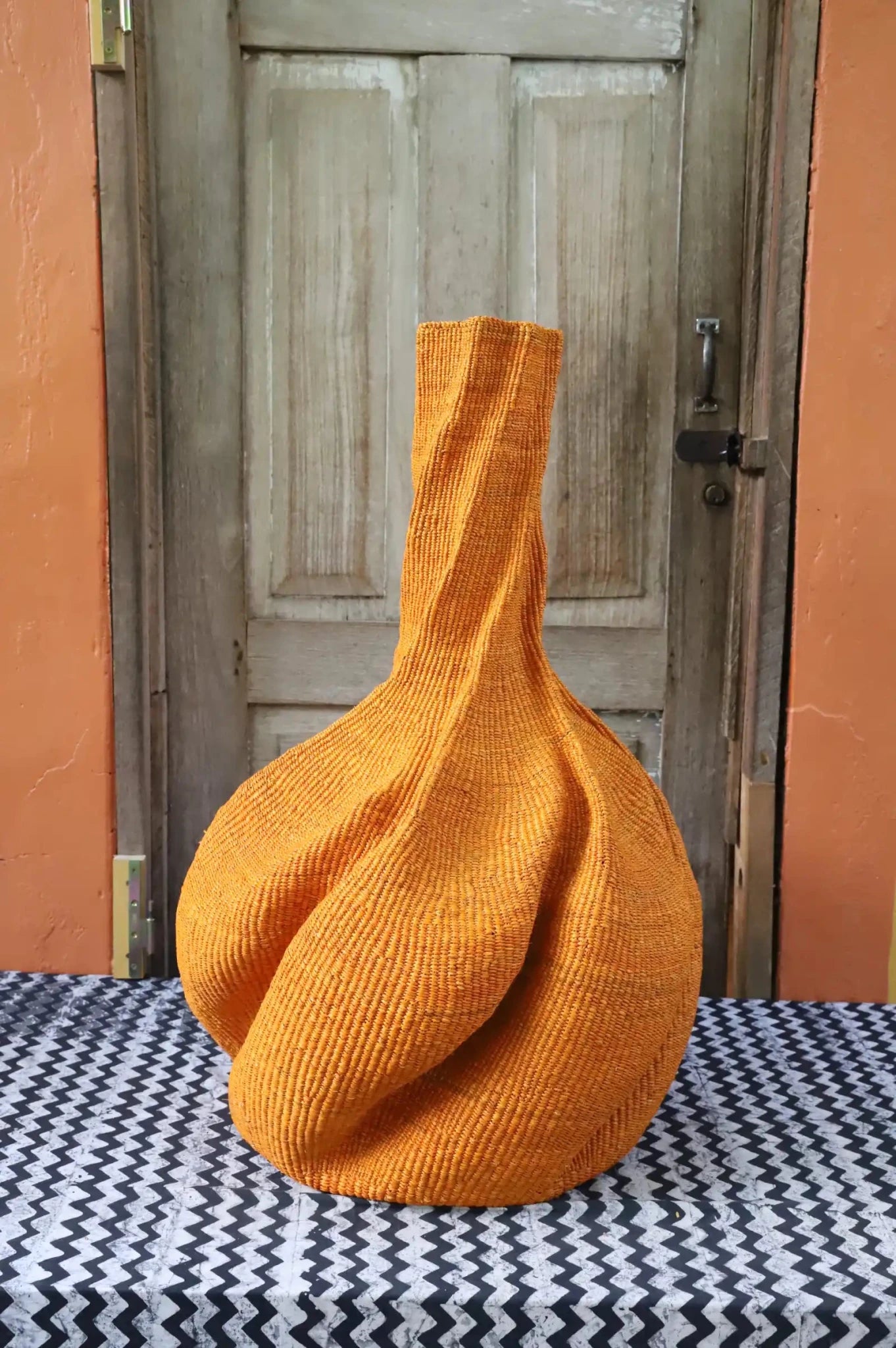 A colourful, handwoven piece with decorative curves sitting on a black and white cloth against a wooden door