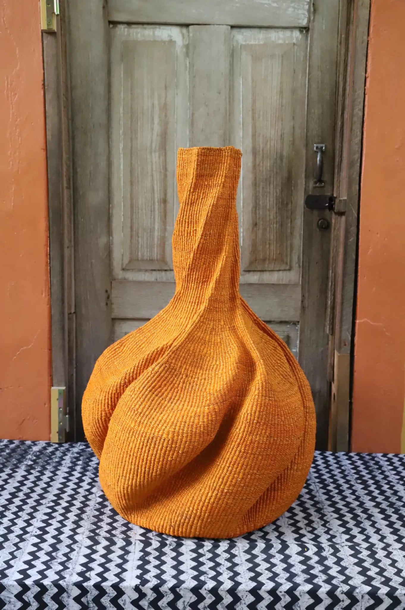A colourful, handwoven piece with decorative curves sitting on a black and white cloth against a wooden door