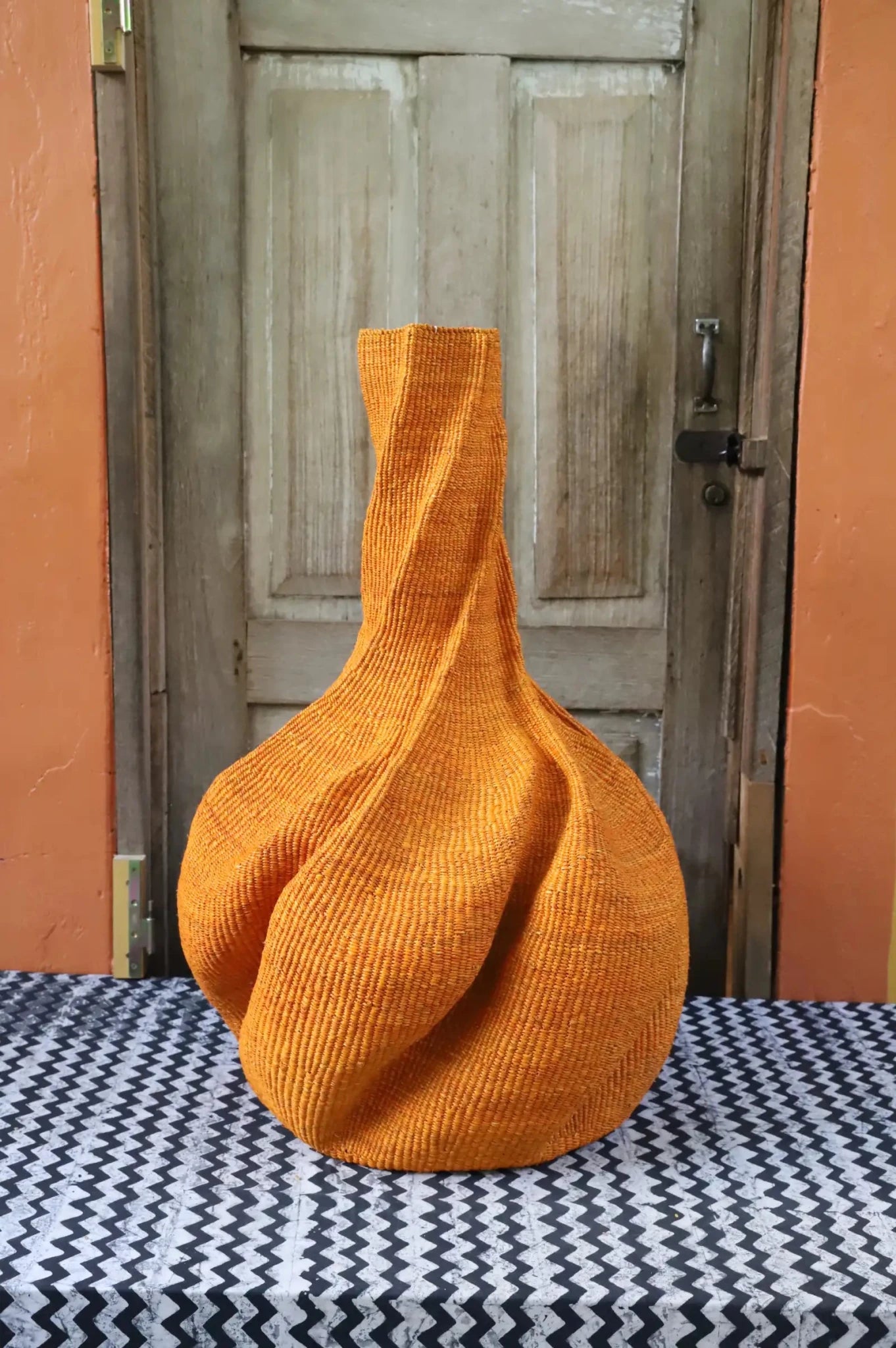A colourful, handwoven piece with decorative curves sitting on a black and white cloth against a wooden door