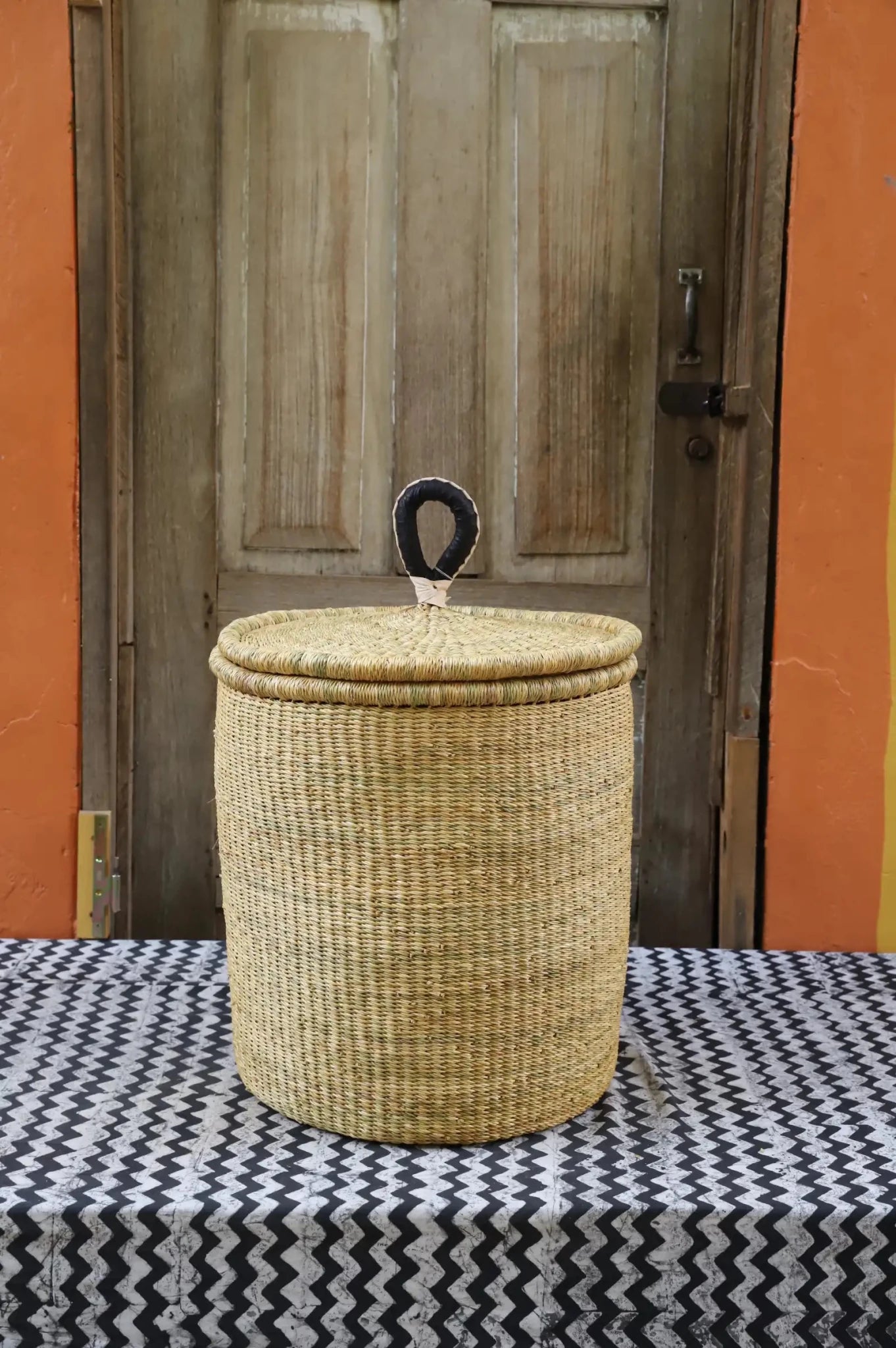 Lidded Laundry Basket with coil (Small) by The Baba Tree. Handwoven elephant grass with leather handle. Premium Bolgatanga artisan decor.