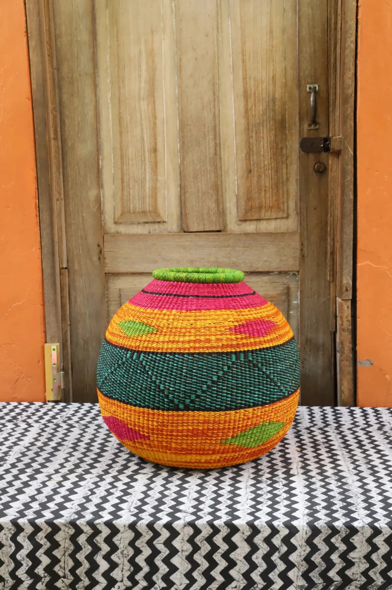 Colorful woven décor basket on a black and white cloth with a wooden door in the background.