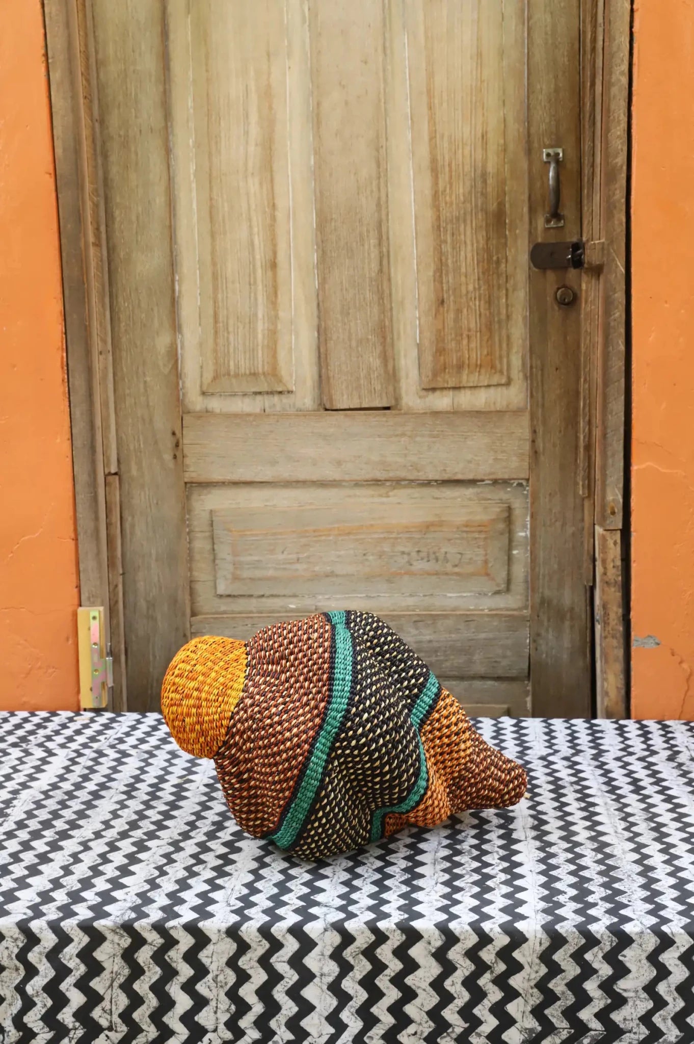 Woven conch piece on a black and white patterned surface with a wooden door in the background.