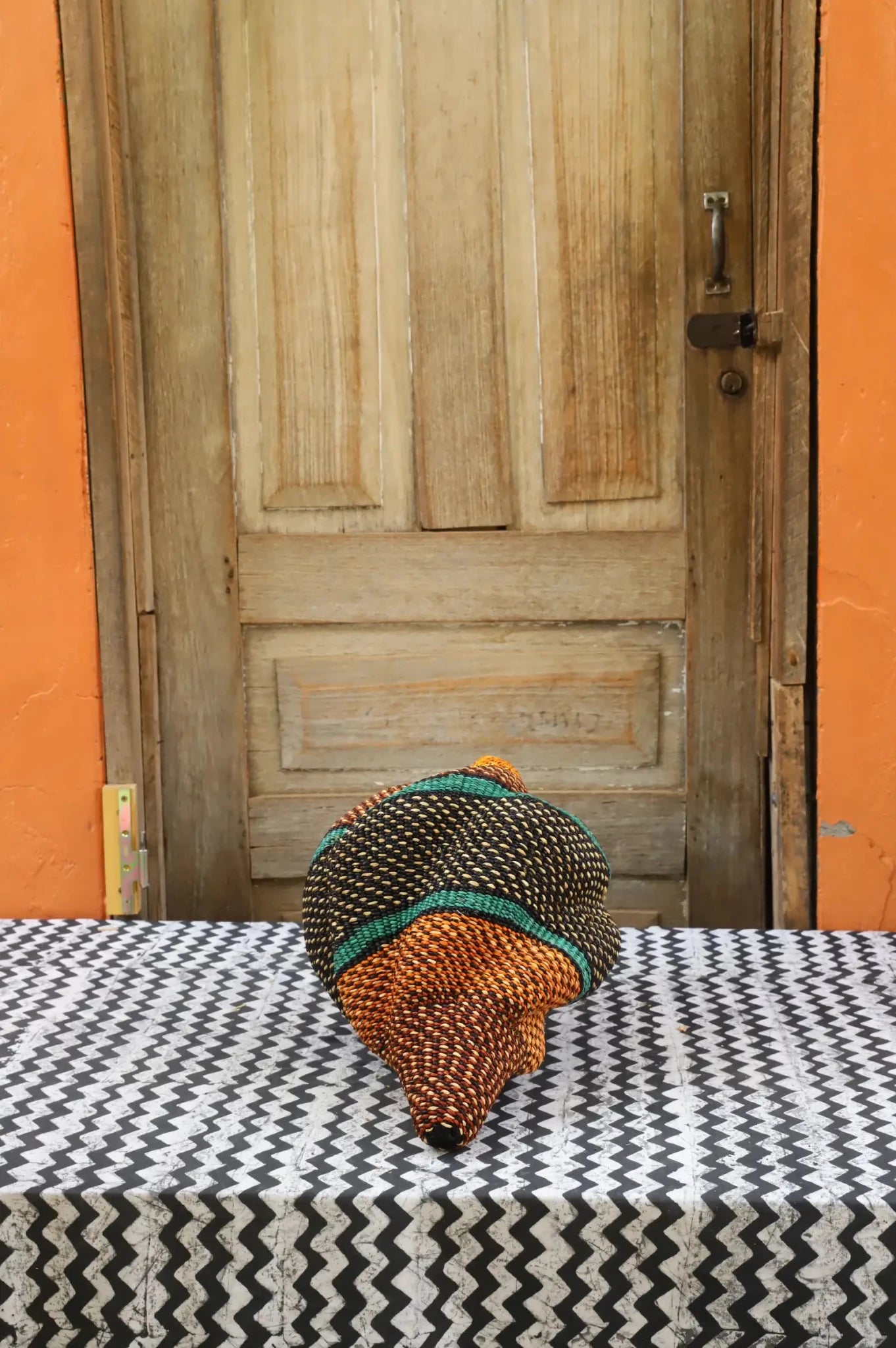 Woven conch piece on a black and white patterned surface with a wooden door in the background.