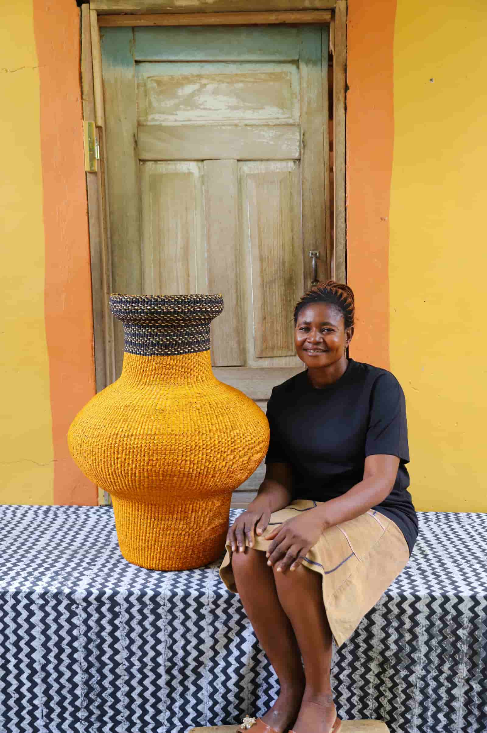 Woman sitting next to a colorful, woven décor piece on a black and white cloth against a wooden door.