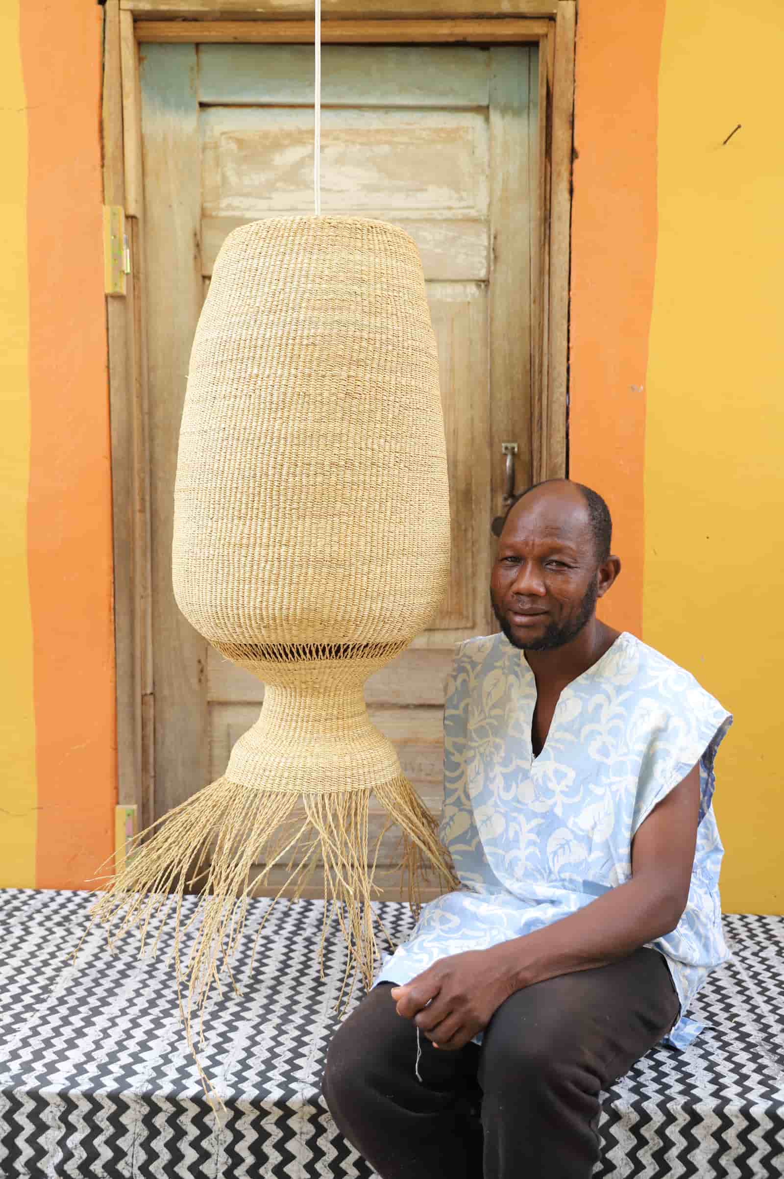 Man sitting on a bench with a woven lamp behind him against a colorful wall.