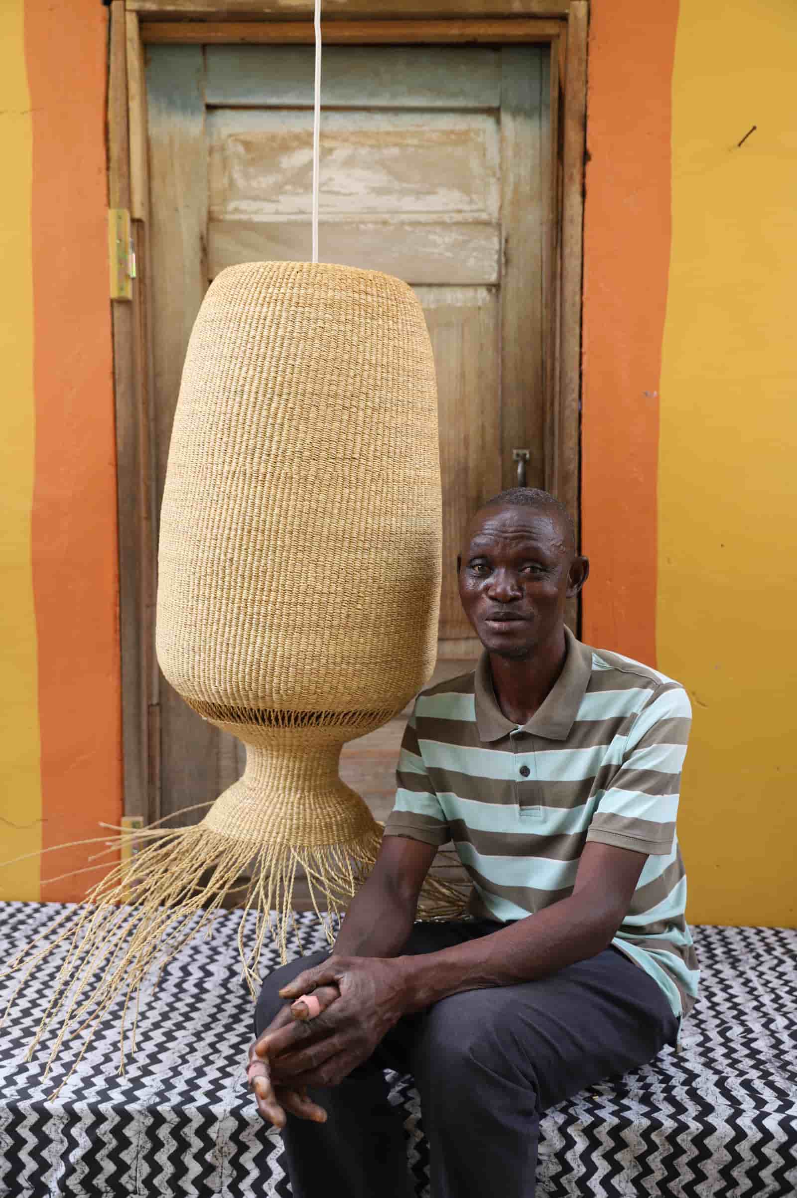 Woven lampshade hanging against a colourful striped wall and wooden door with man sitting on black and white cloth 
