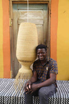 Man sitting next to a large woven lamp against a colorful wall.