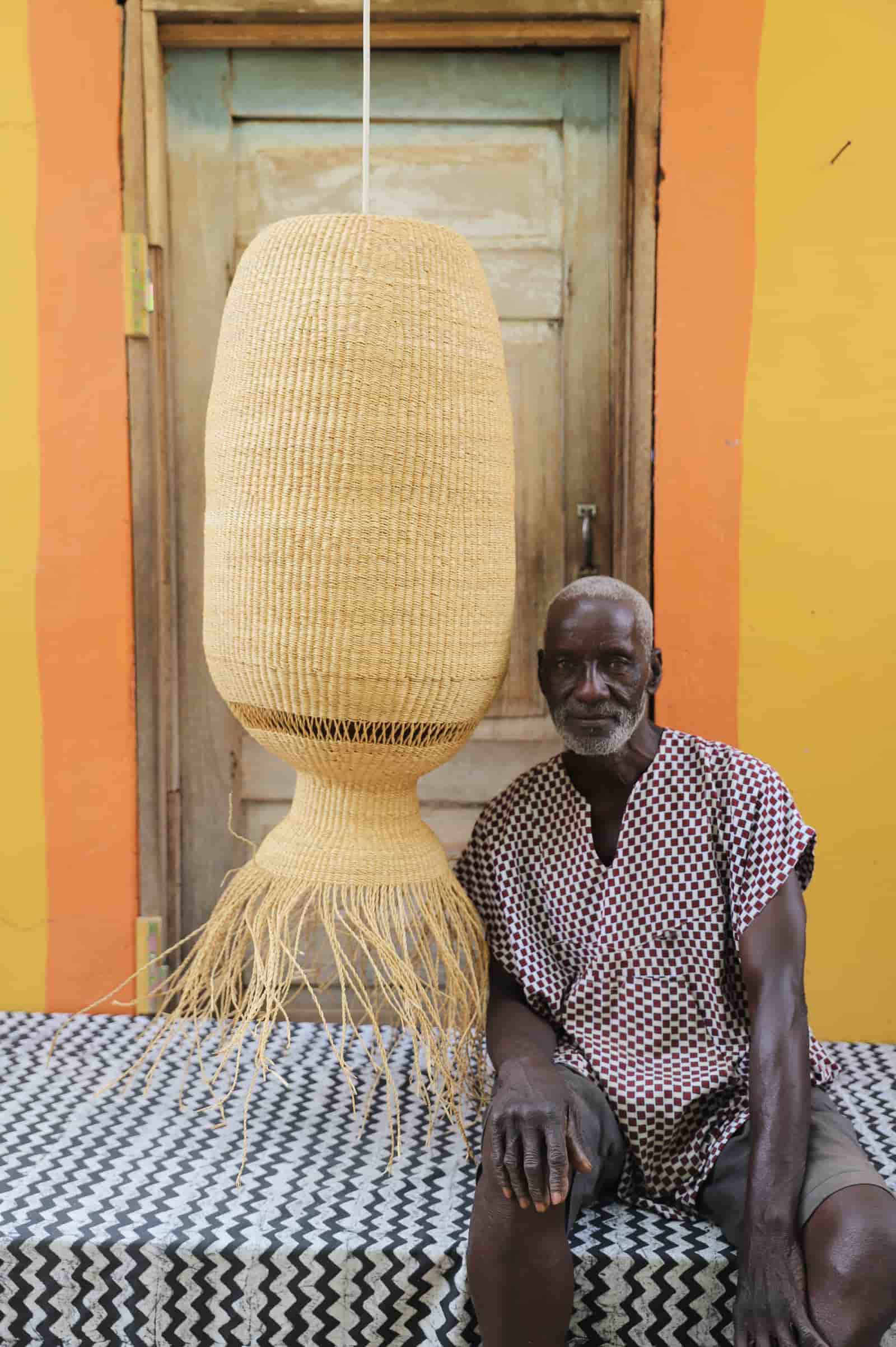 Man sitting on a bench next to a large woven lamp against a colorful wall.