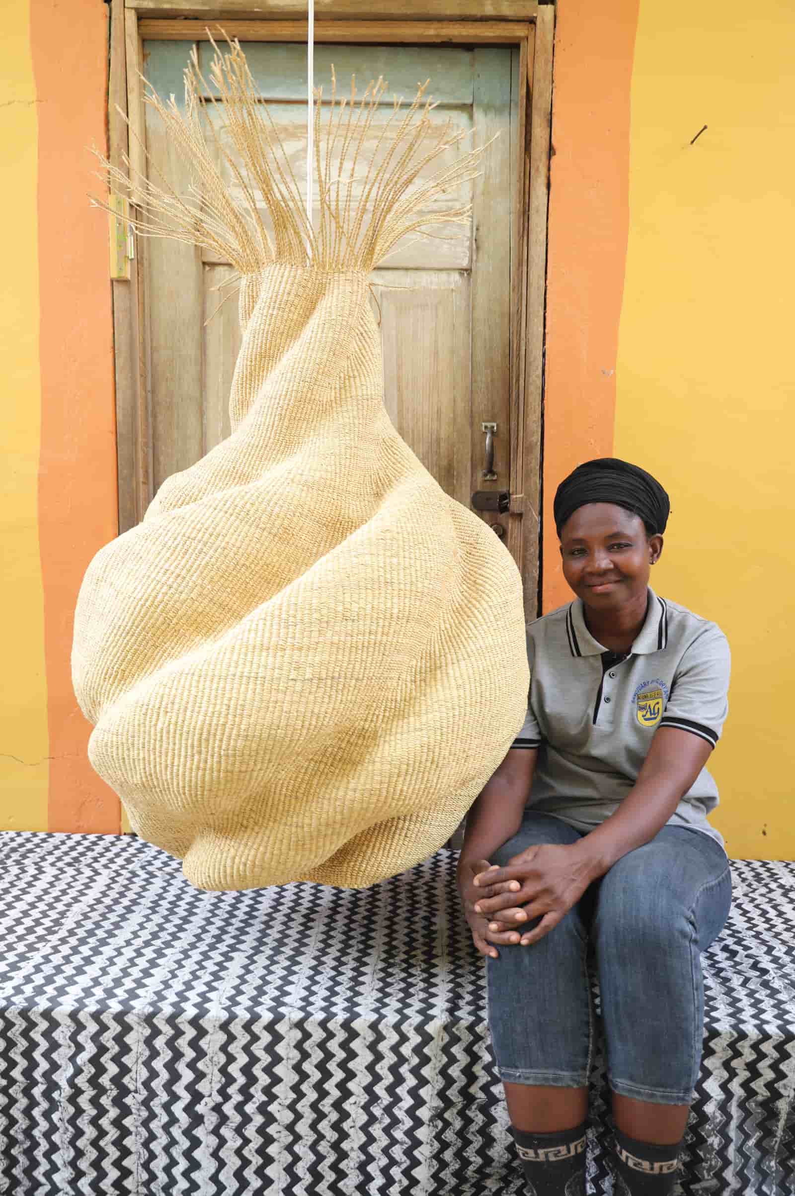 Woman sitting on a black and white next to a large woven basket against a yellow wall.