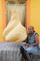 Woman sitting on a black and white cloth  with a large woven basket in front of a yellow wall.