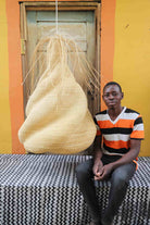 Man sitting on a black and white cloth  with a large woven basket behind him against a colorful wall.