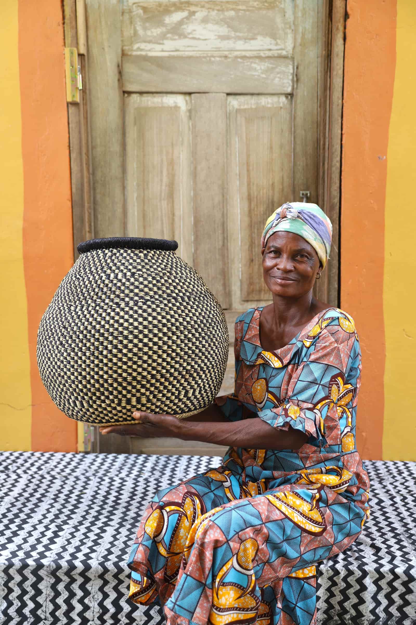 Woman holding a checkered woven décor basket on a black and white cloth with a wooden door in the background.