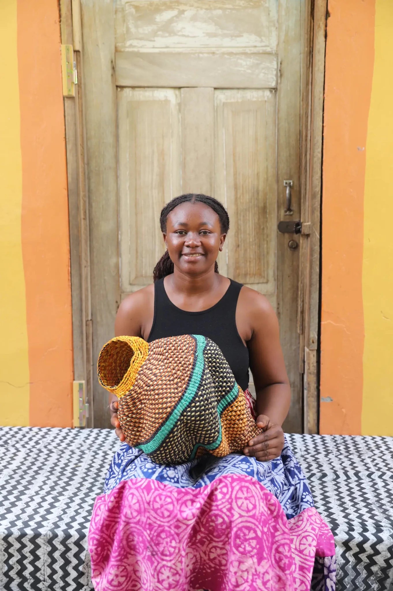 Woman holding a woven conch piece on a black and white patterned surface with a wooden door in the background.