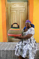 Woman holding a colorful woven basket in front of a wooden door with an orange wall.