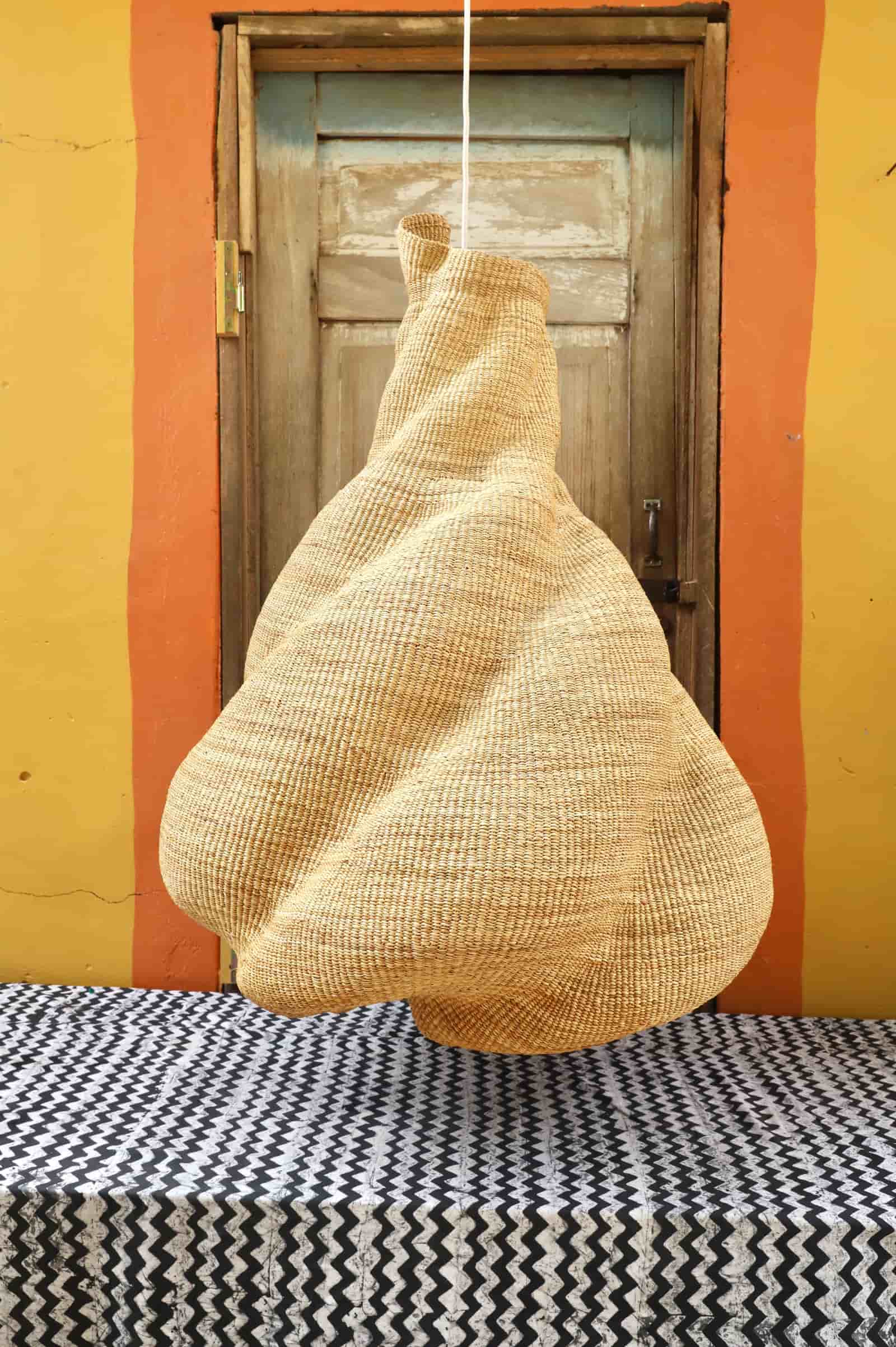 Woven basket hanging against a yellow wall with a wooden door.