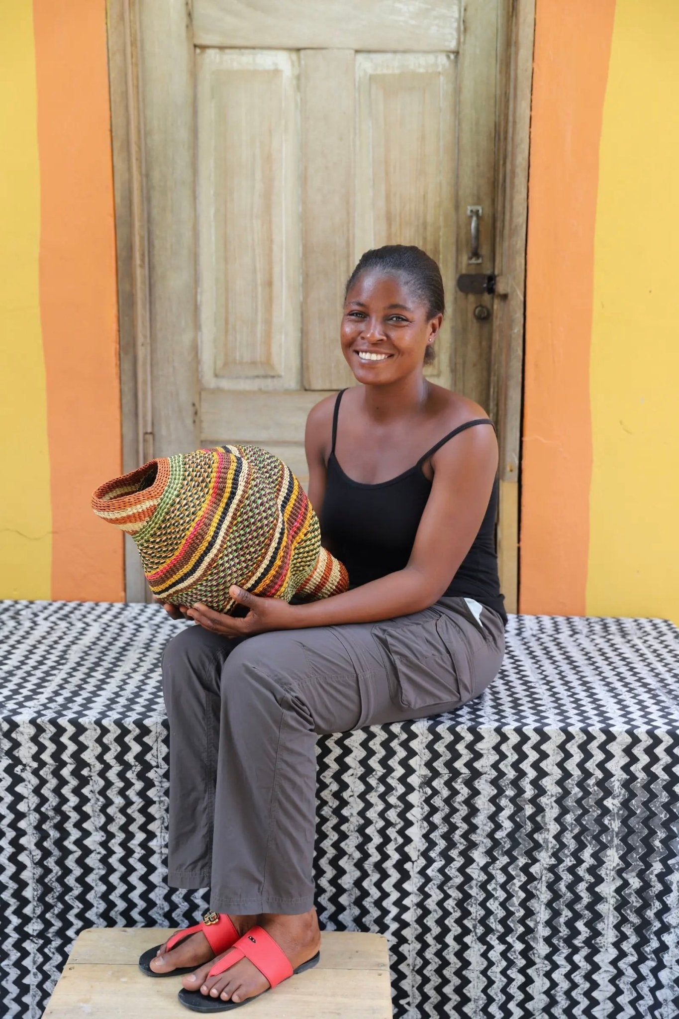 Woman holding a woven conch piece on a black and white patterned surface with a wooden door in the background.