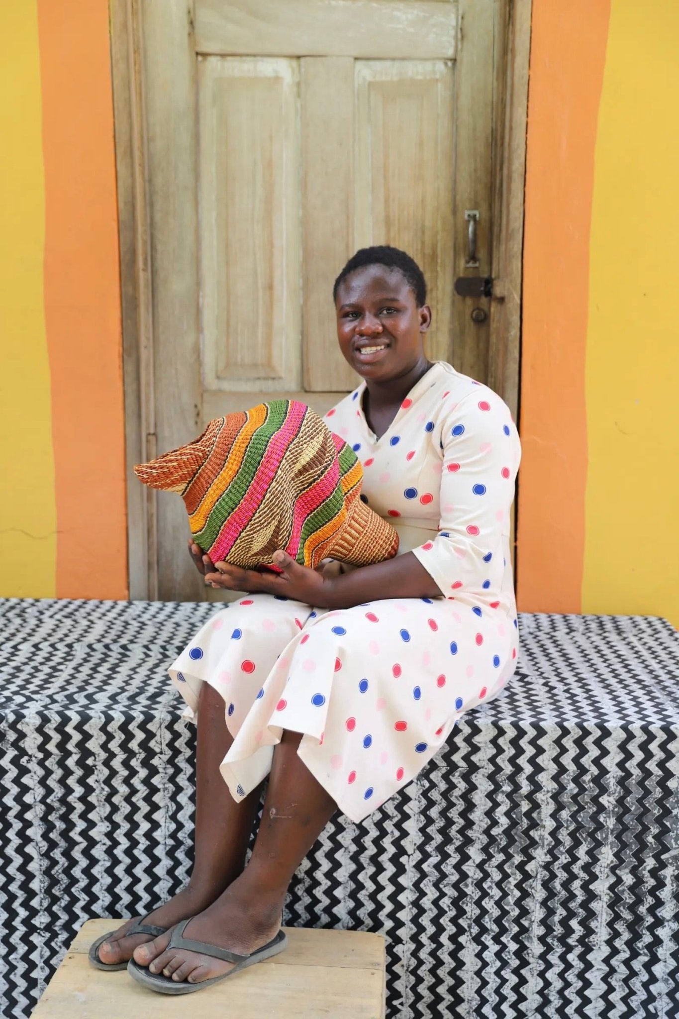 Woman holding a woven conch piece on a black and white patterned surface with a wooden door in the background.