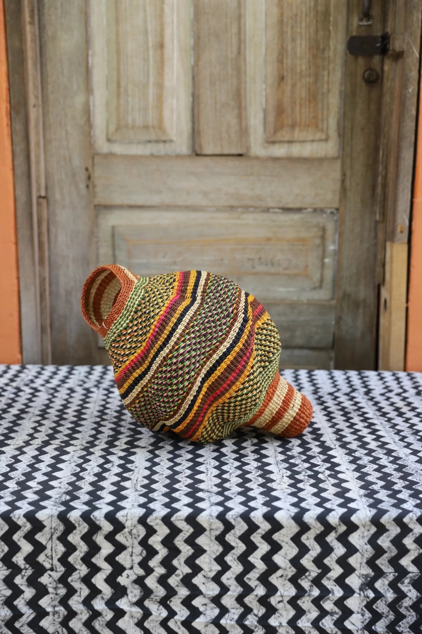 Colorful conch-shaped piece on a black and white cloth against a wooden door.