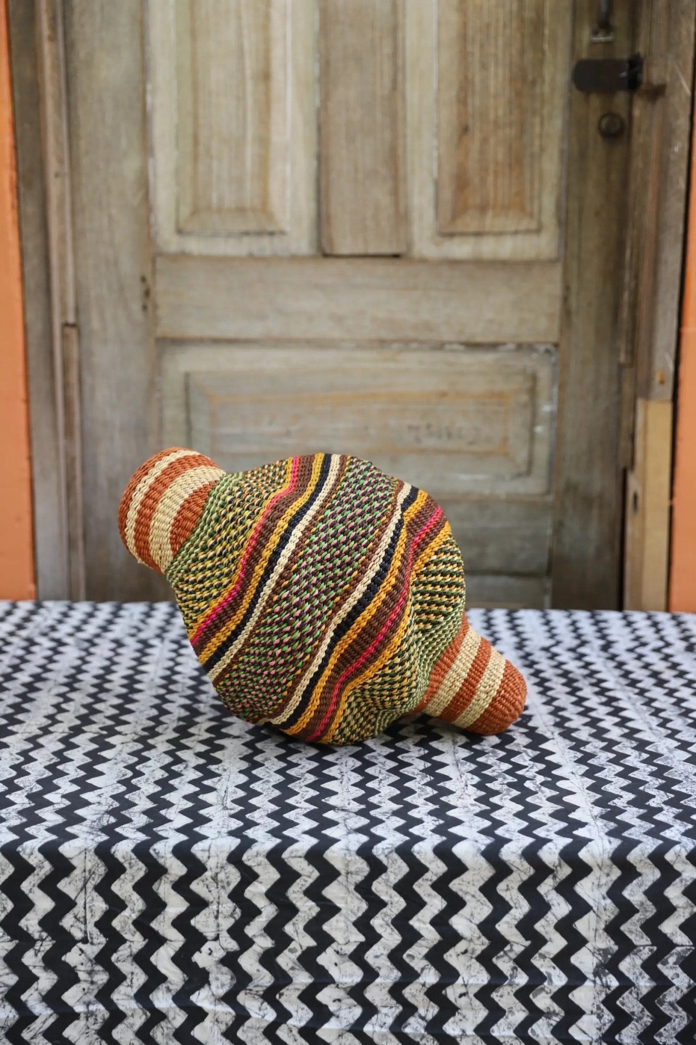 Woven conch piece on a black and white patterned surface with a wooden door in the background.