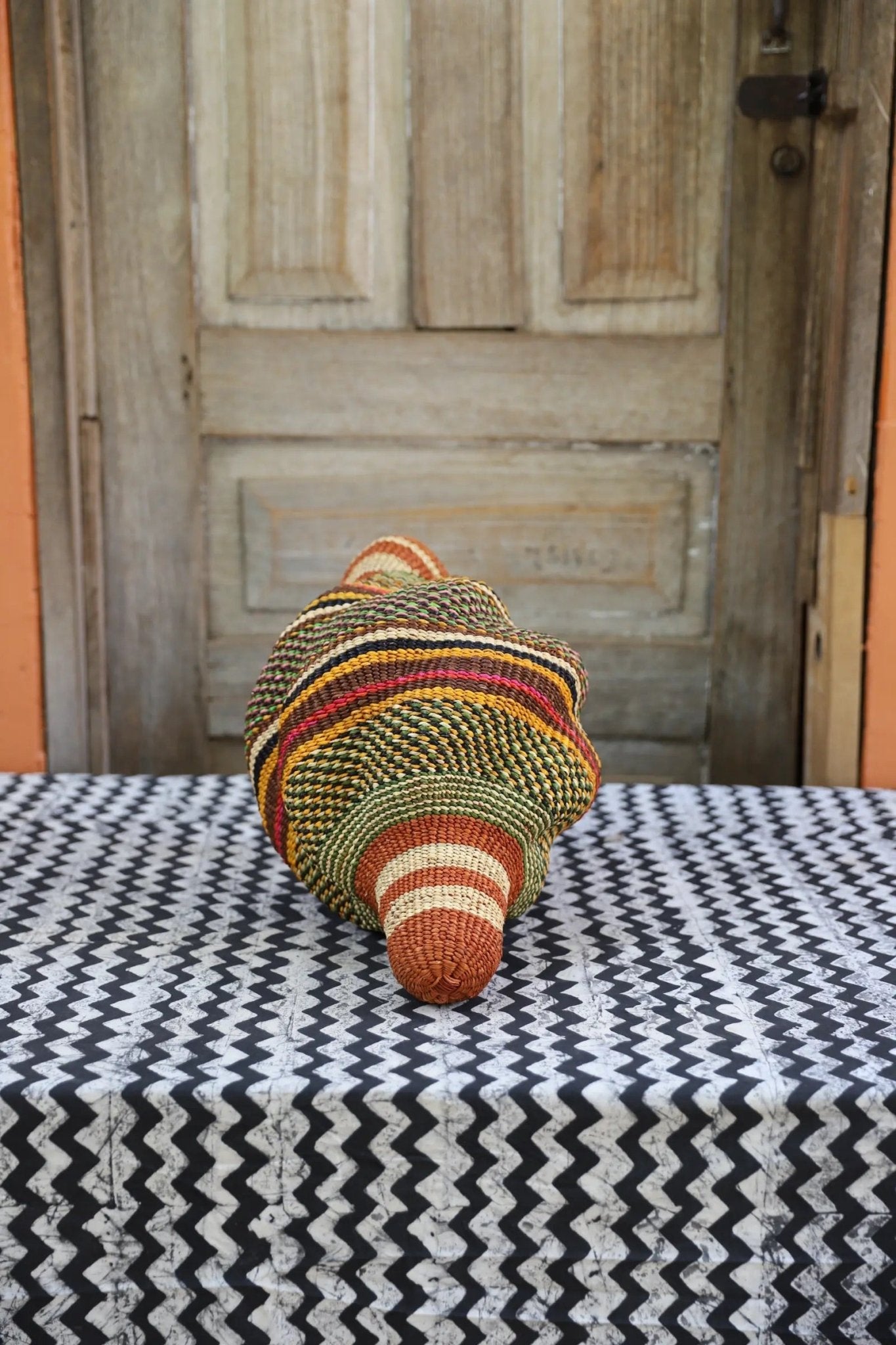 Woven conch piece on a black and white patterned surface with a wooden door in the background.