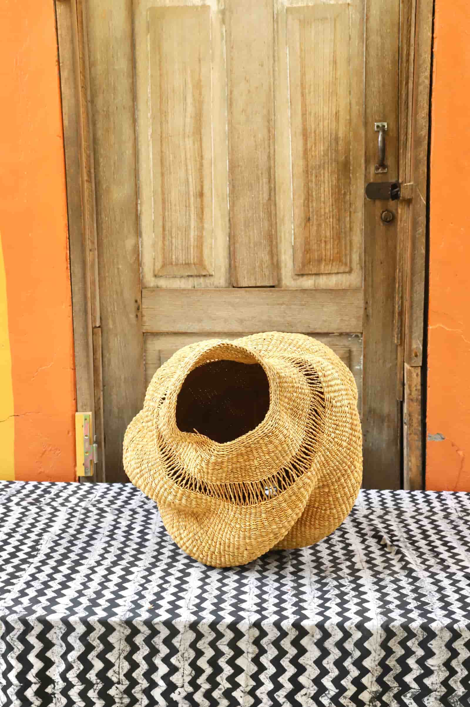Woven conch lampshade on a table with an orange wall and wooden door in the background
