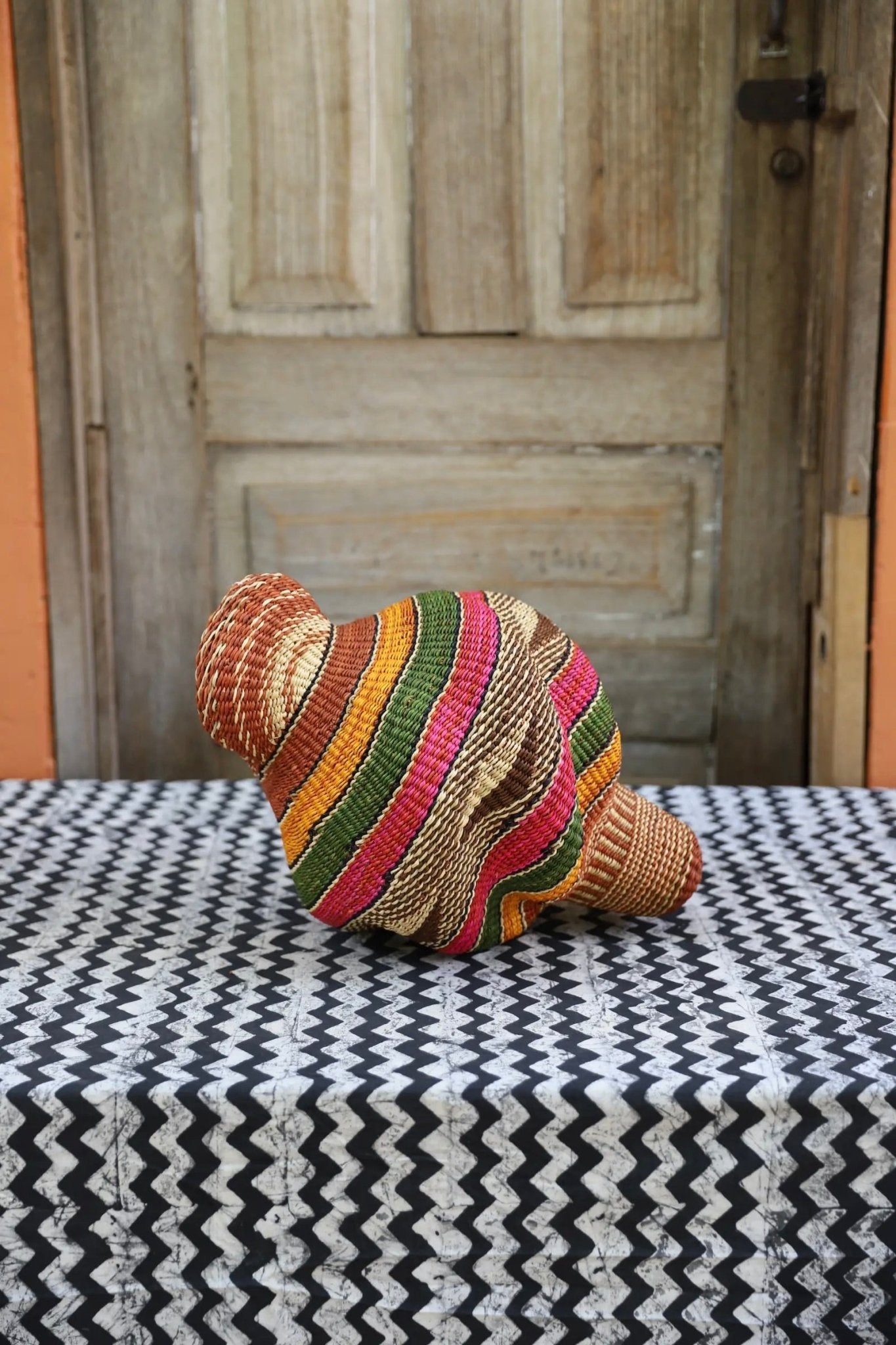 Colorful woven conch piece on a black and white patterned surface with a wooden door in the background.