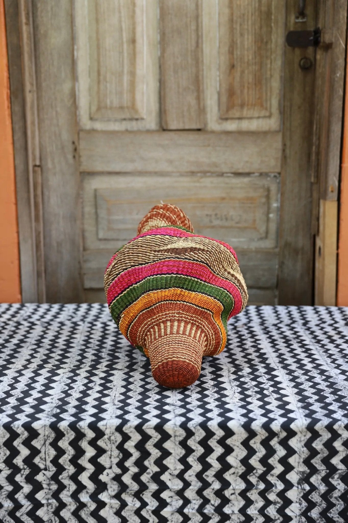 Woven conch piece on a black and white patterned surface with a wooden door in the background.